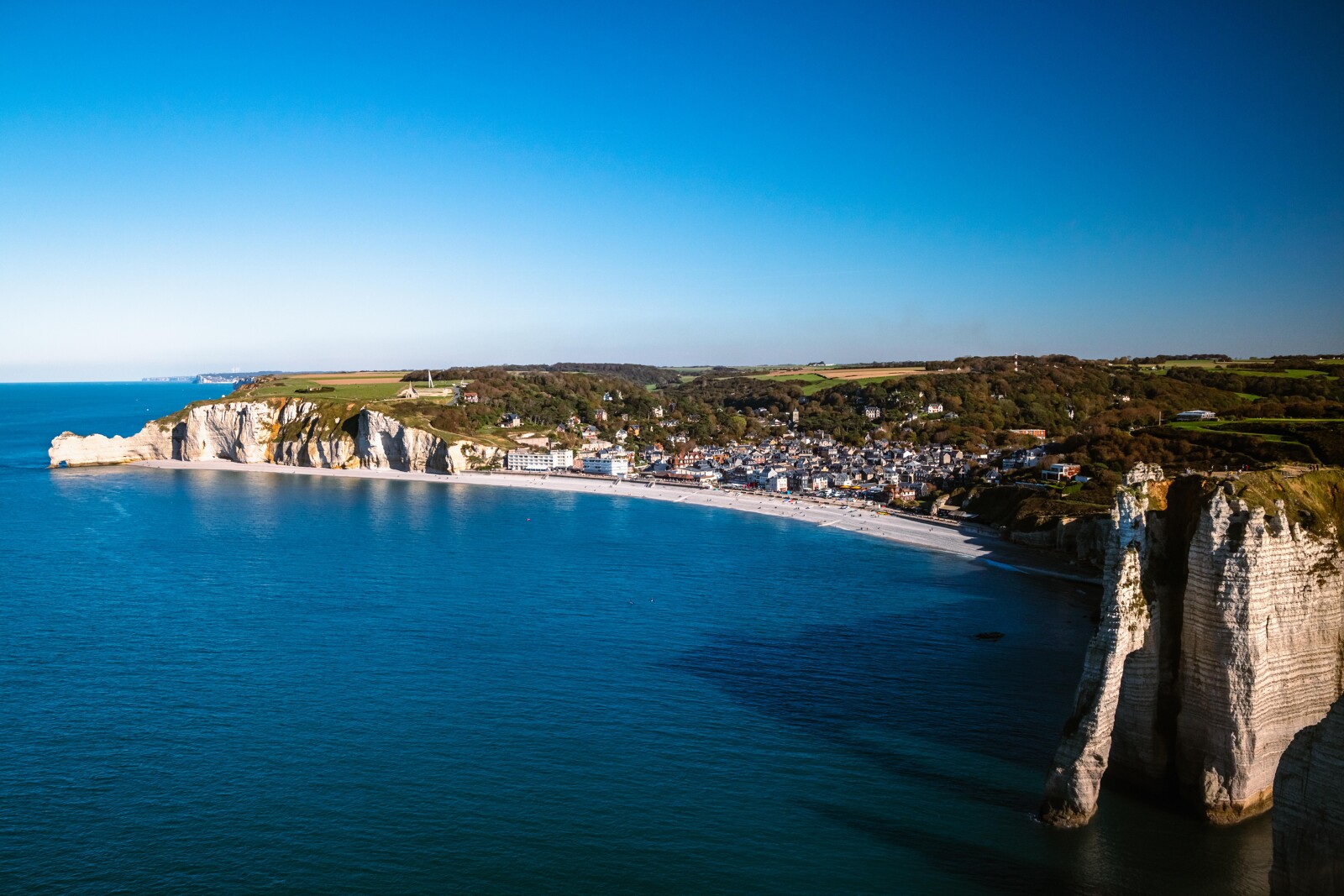 Panorama aérien sur Étretat et sa plage de galets, entourée des falaises blanches emblématiques de la Côte d’Albâtre en Normandie.