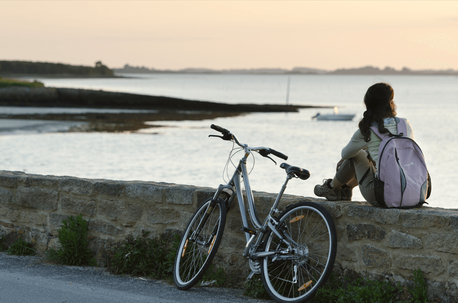 GR34 : Une randonneuse assise sur un muret prêt de son vélo admire le golfe du Morbihan