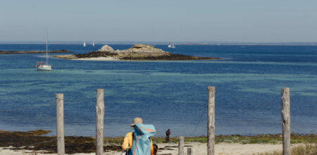 Randonneur avec sac à dos descendant vers une plage bretonne aux eaux turquoise en septembre