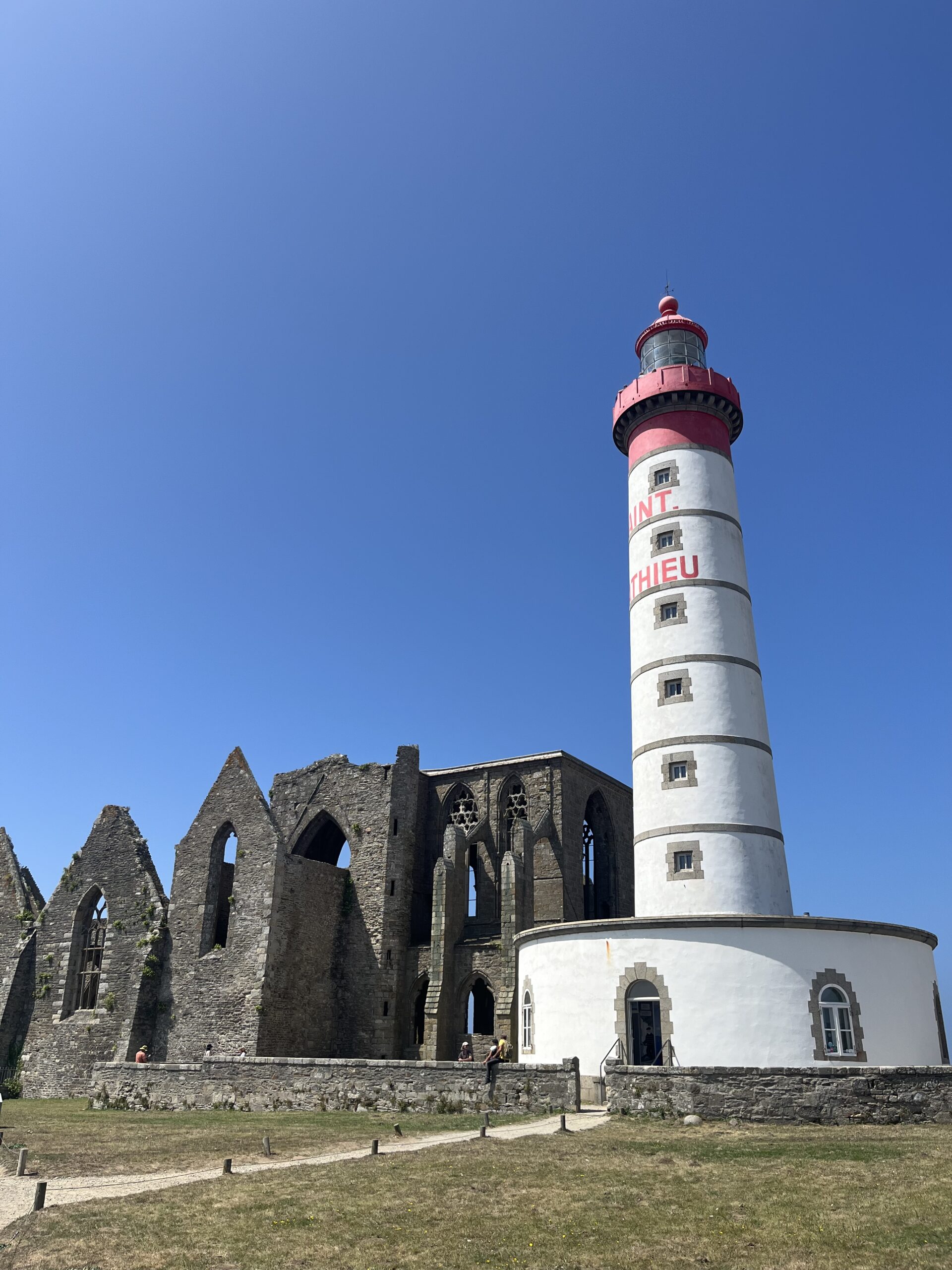 Que faire dans les Abers ? : Phare de Saint-Mathieu devant les ruines de l’abbaye, sous un ciel bleu éclatant.