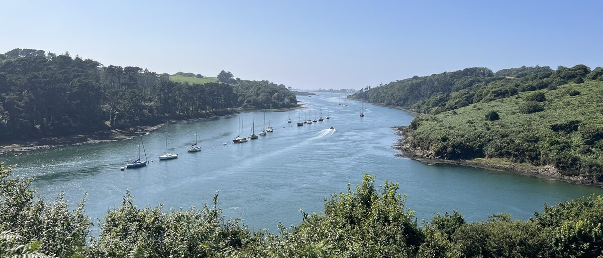 Aber breton serpentant entre collines verdoyantes avec voiliers.
