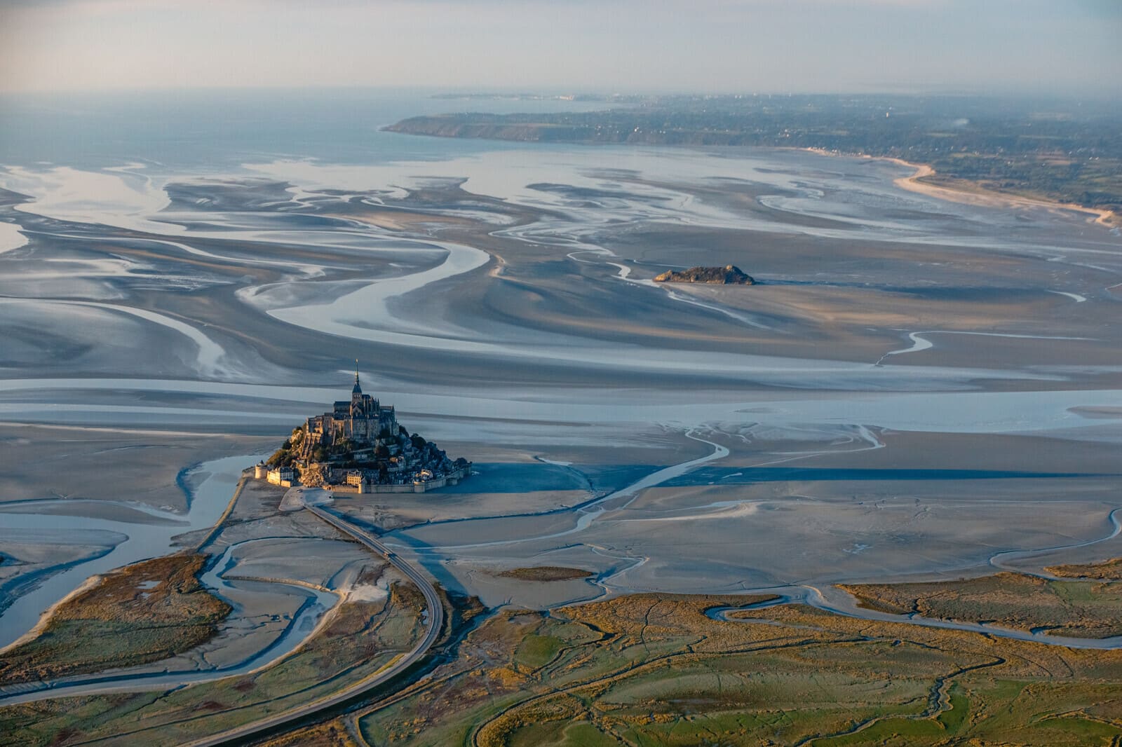 Vue aérienne du Mont-Saint-Michel entouré par les méandres de sa baie à marée basse, entre Bretagne et Normandie