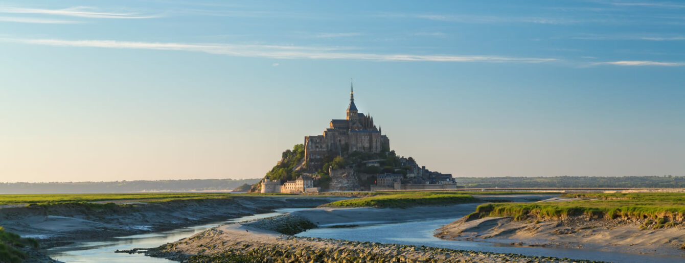 Vue panoramique du Mont-Saint-Michel entouré de la baie et des canaux à marée basse au lever du jour