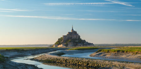 Vue panoramique du Mont-Saint-Michel entouré de la baie et des canaux à marée basse au lever du jour